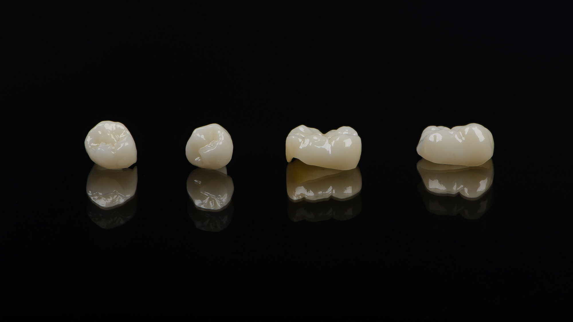 Corone anatomiche in ceramica e zirconio, riprese in macro su fondo nero.
